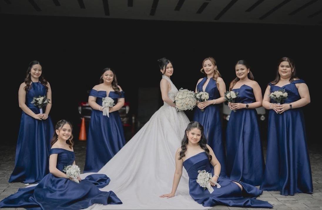 Bride in white gown surrounded by bridesmaids wearing royal blue dresses holding bouquets.