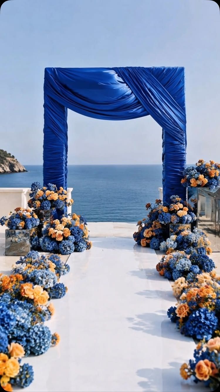 Royal blue and orange floral arrangements lining a white aisle under a blue arch.