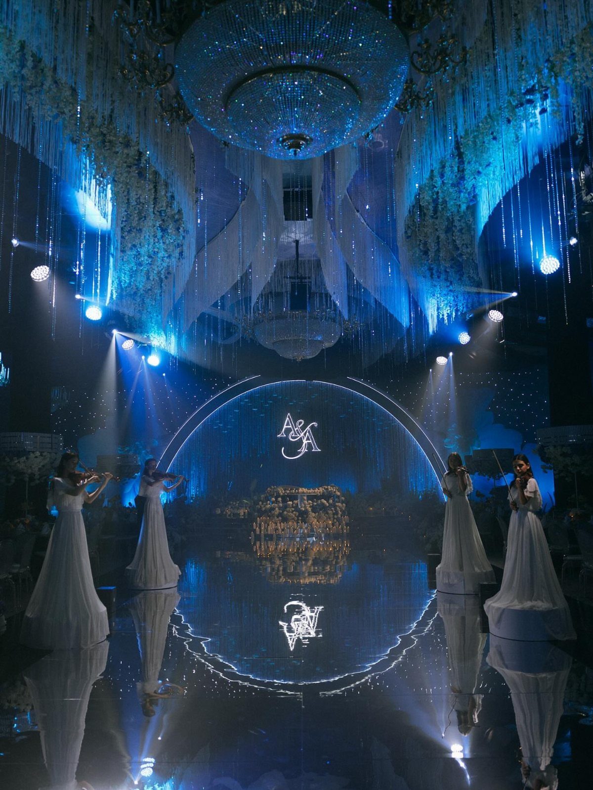 Grand event hall with royal blue lighting, white gowns, and a gold monogram.
