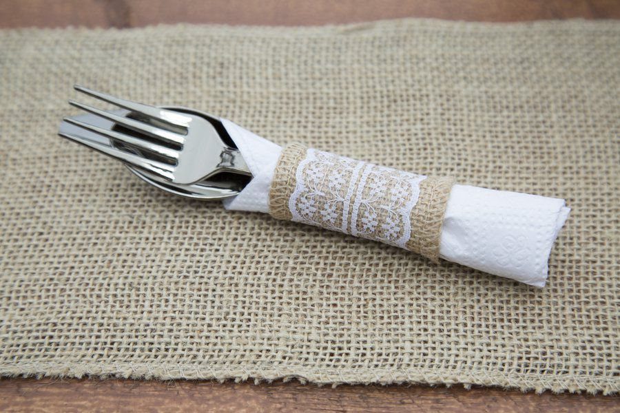 Silverware wrapped in a white napkin with a burlap and lace band.