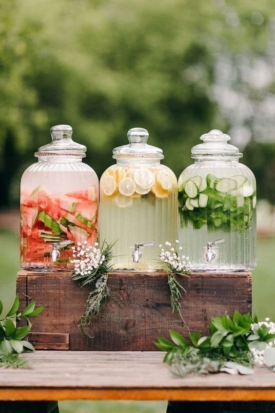 Three glass drink dispensers with infused water on a rustic wooden crate outdoors.