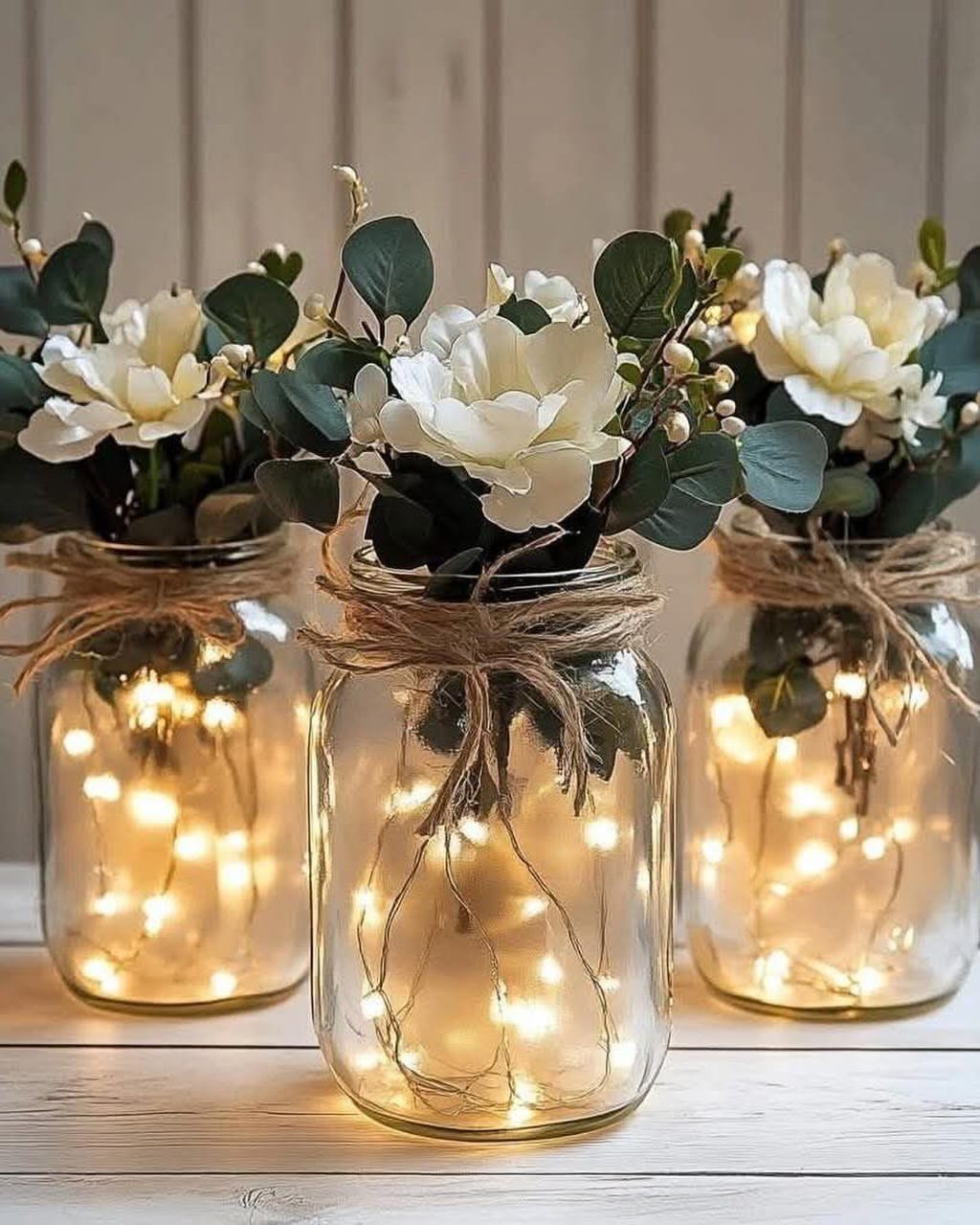 Mason jar vases with white flowers and glowing fairy lights tied with twine.