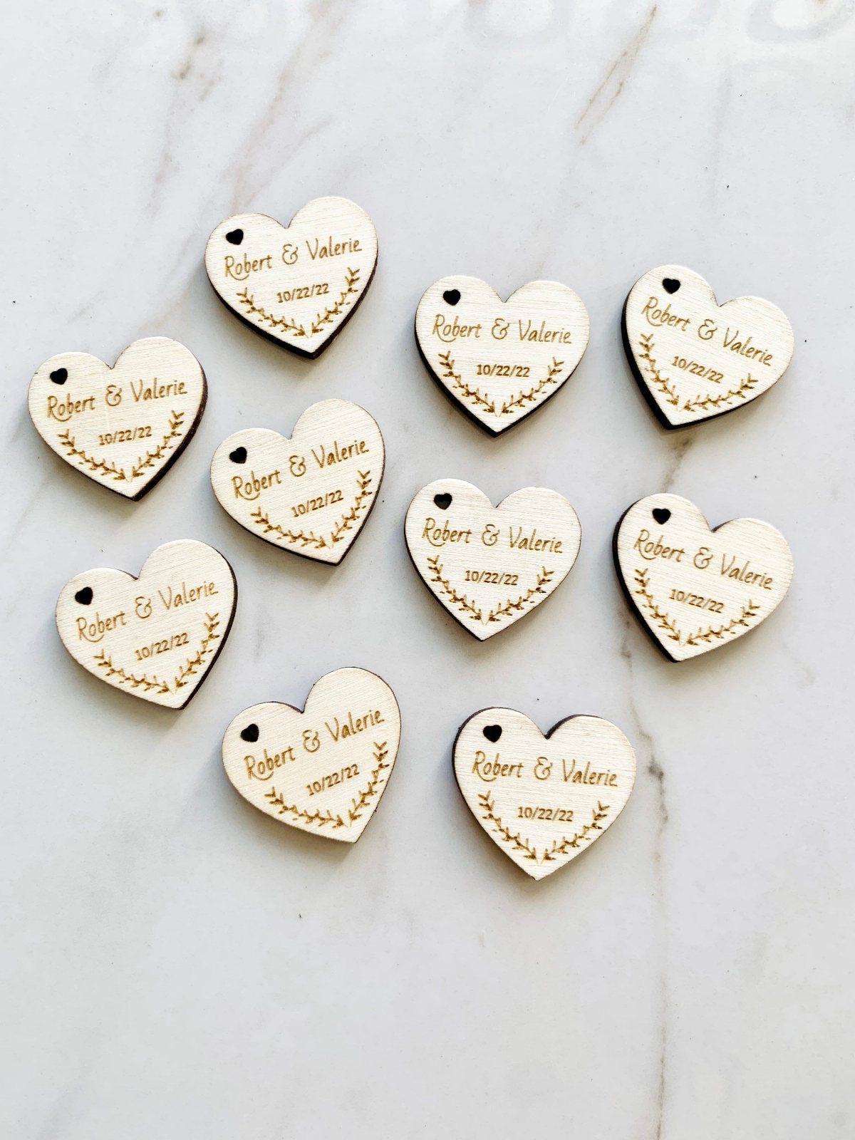 Heart-shaped wooden tokens engraved with names and a wedding date on marble.
