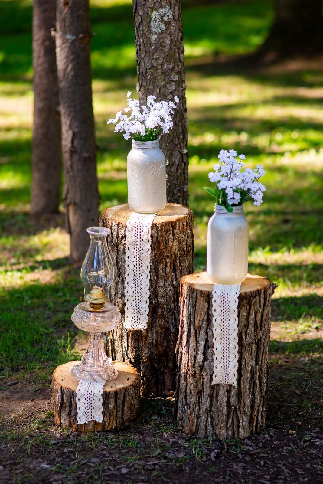 Tree stump stands holding white flowers in mason jars and a vintage lamp.