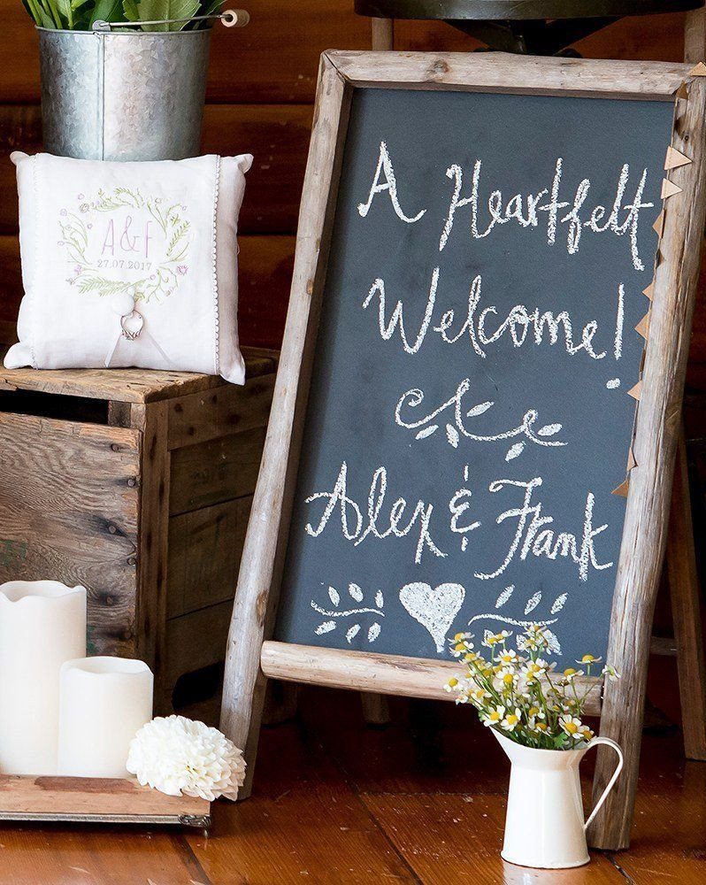 Wooden-framed chalkboard welcome sign for Alex and Frank with rustic wedding decorations.