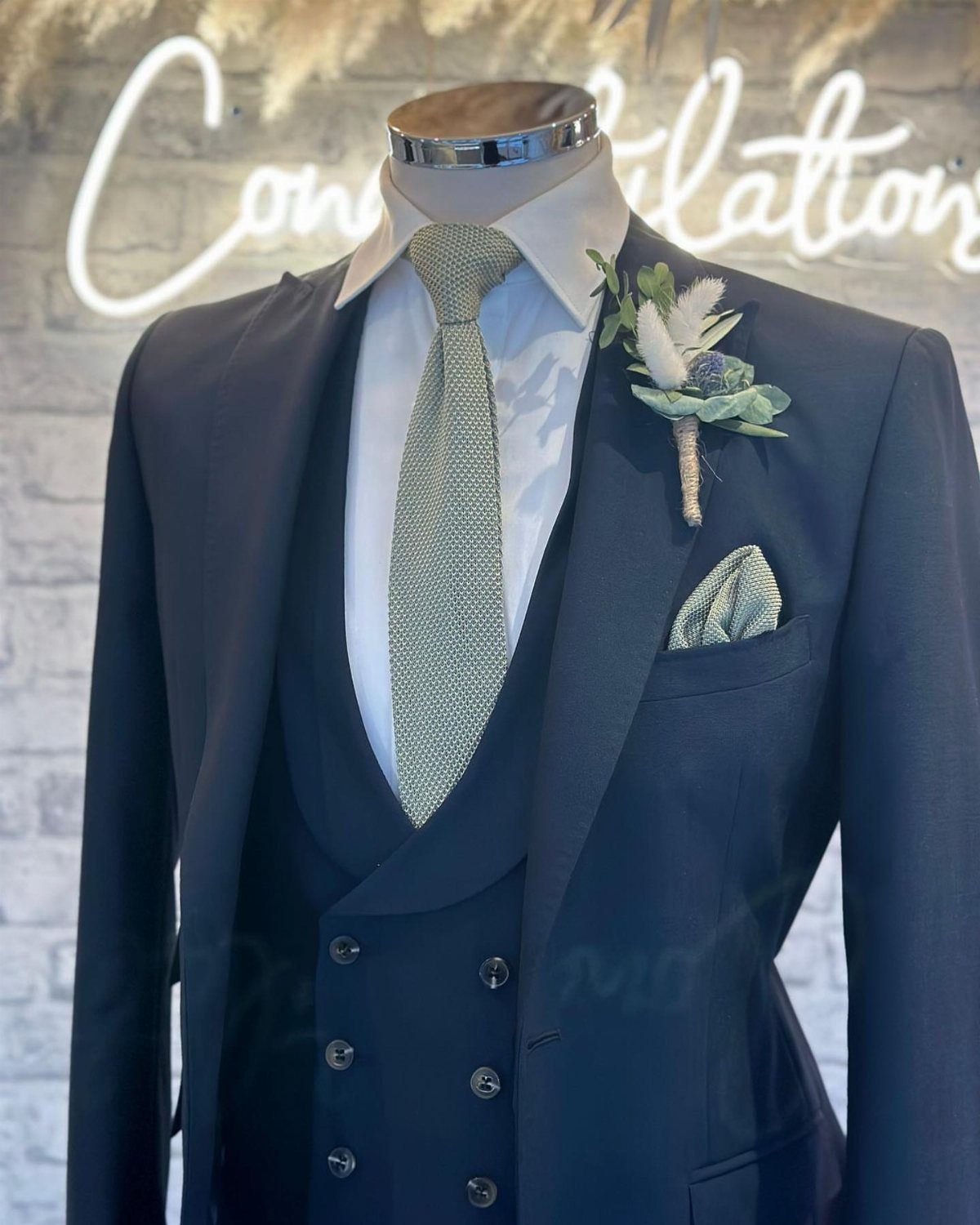 Navy blue three-piece suit with sage green tie, pocket square, and floral boutonniere.