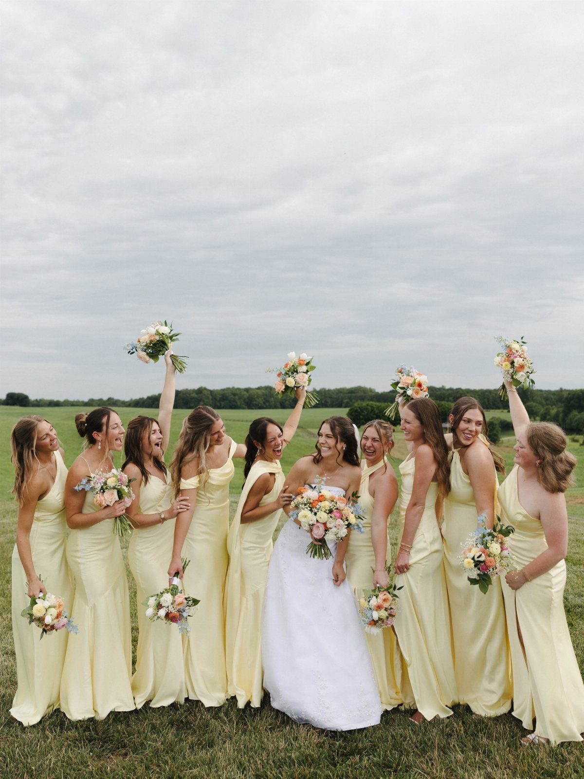 Bride in white gown with bridesmaids in pale yellow dresses in a field