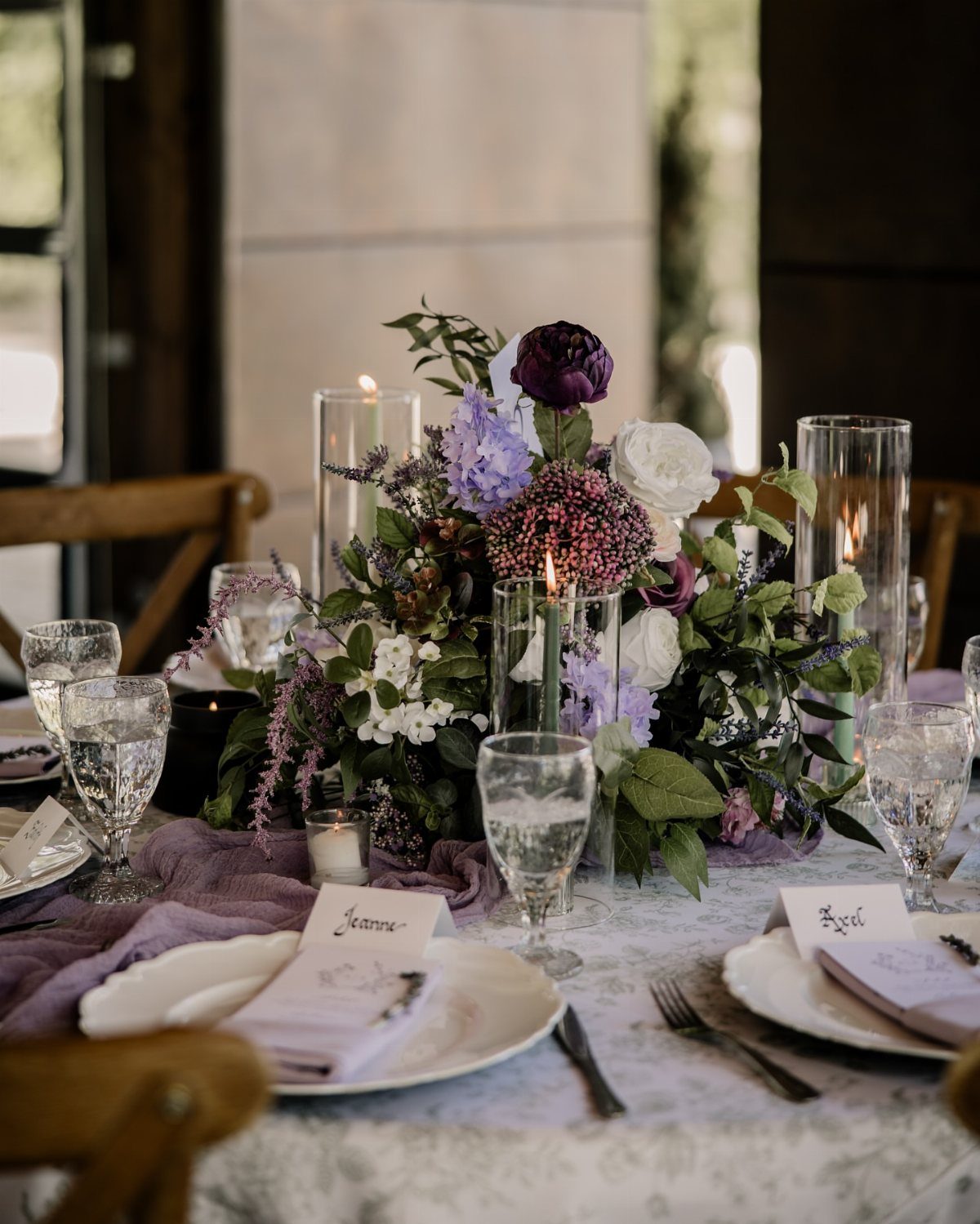 Floral centerpiece with lavender and white flowers and sage green leaves on a table.