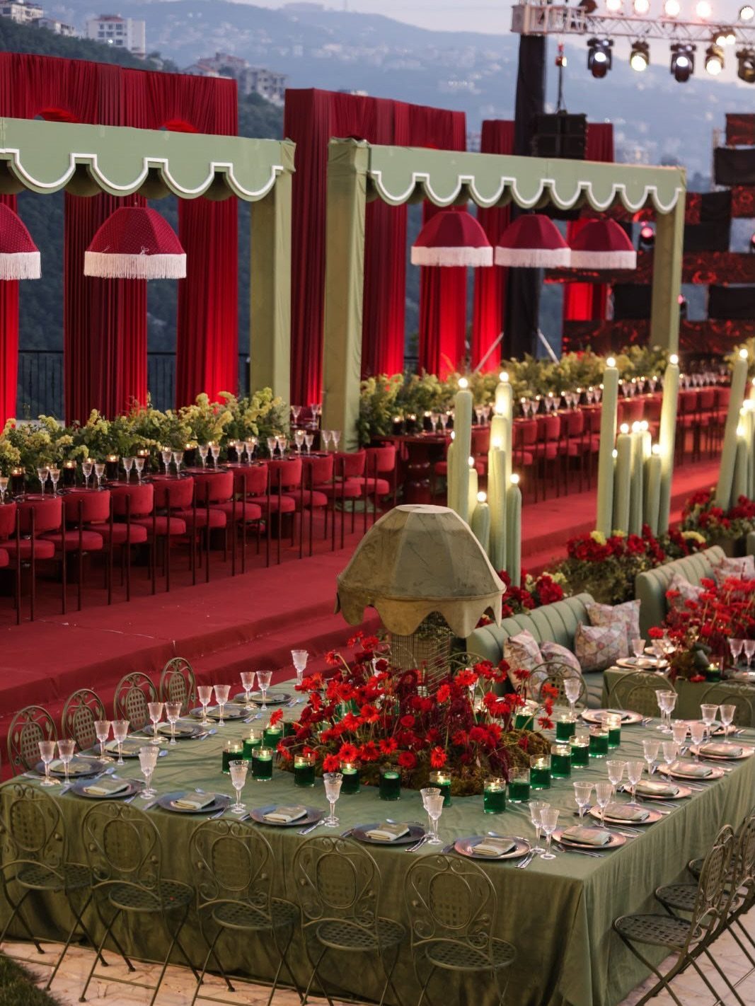 Sage green table and red floral arrangements at an outdoor event with red curtains.