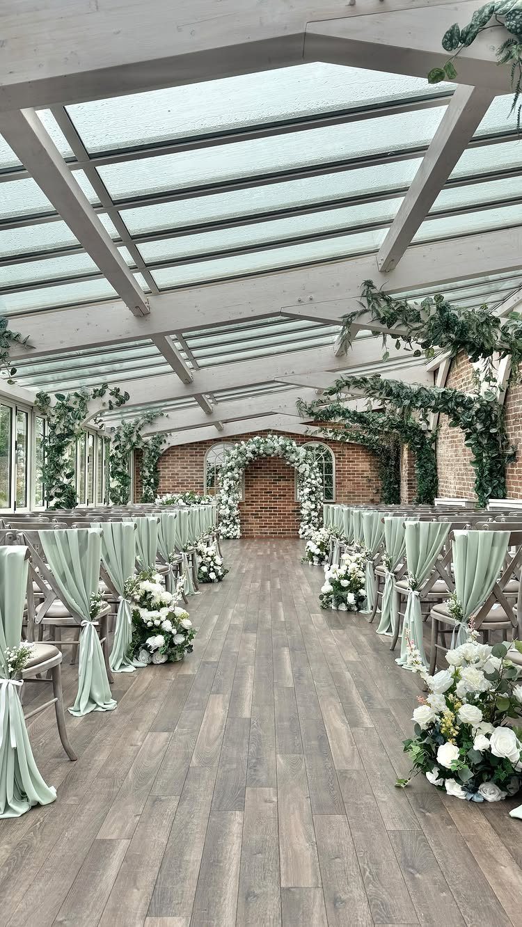 Wedding ceremony setup with sage green chair sashes and white flowers in a conservatory