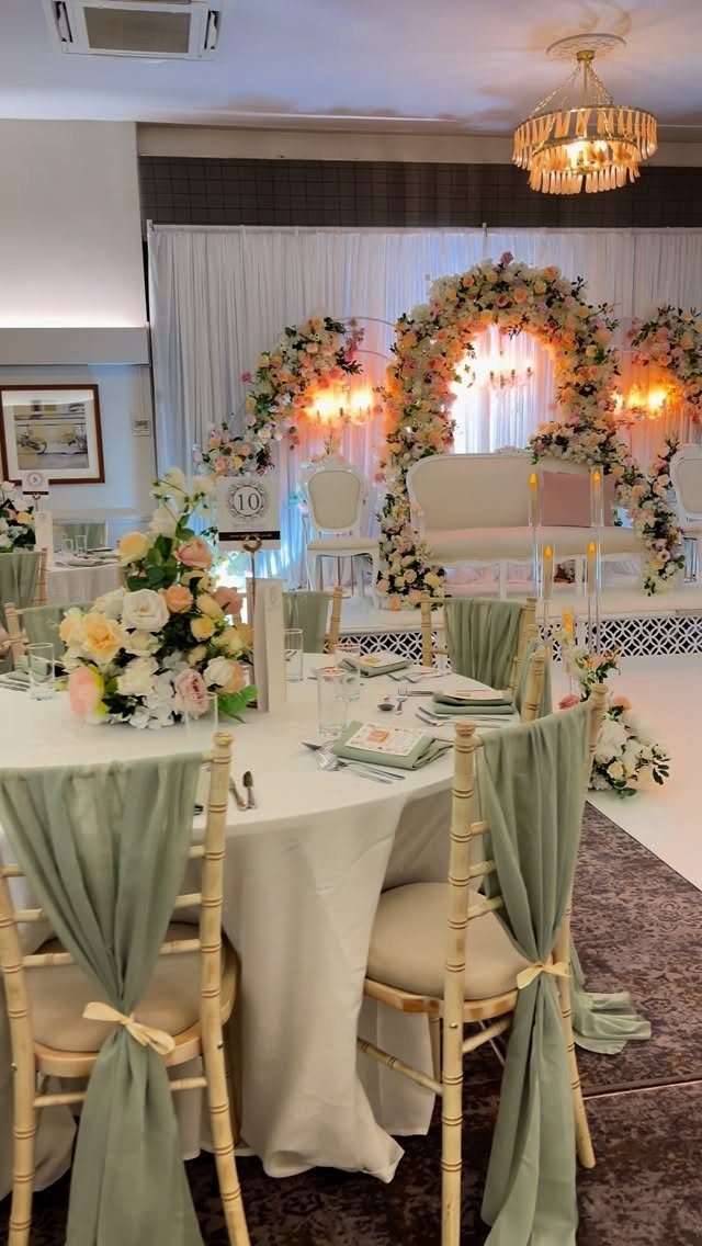 Wedding reception with sage green chair sashes and blush pink floral archway
