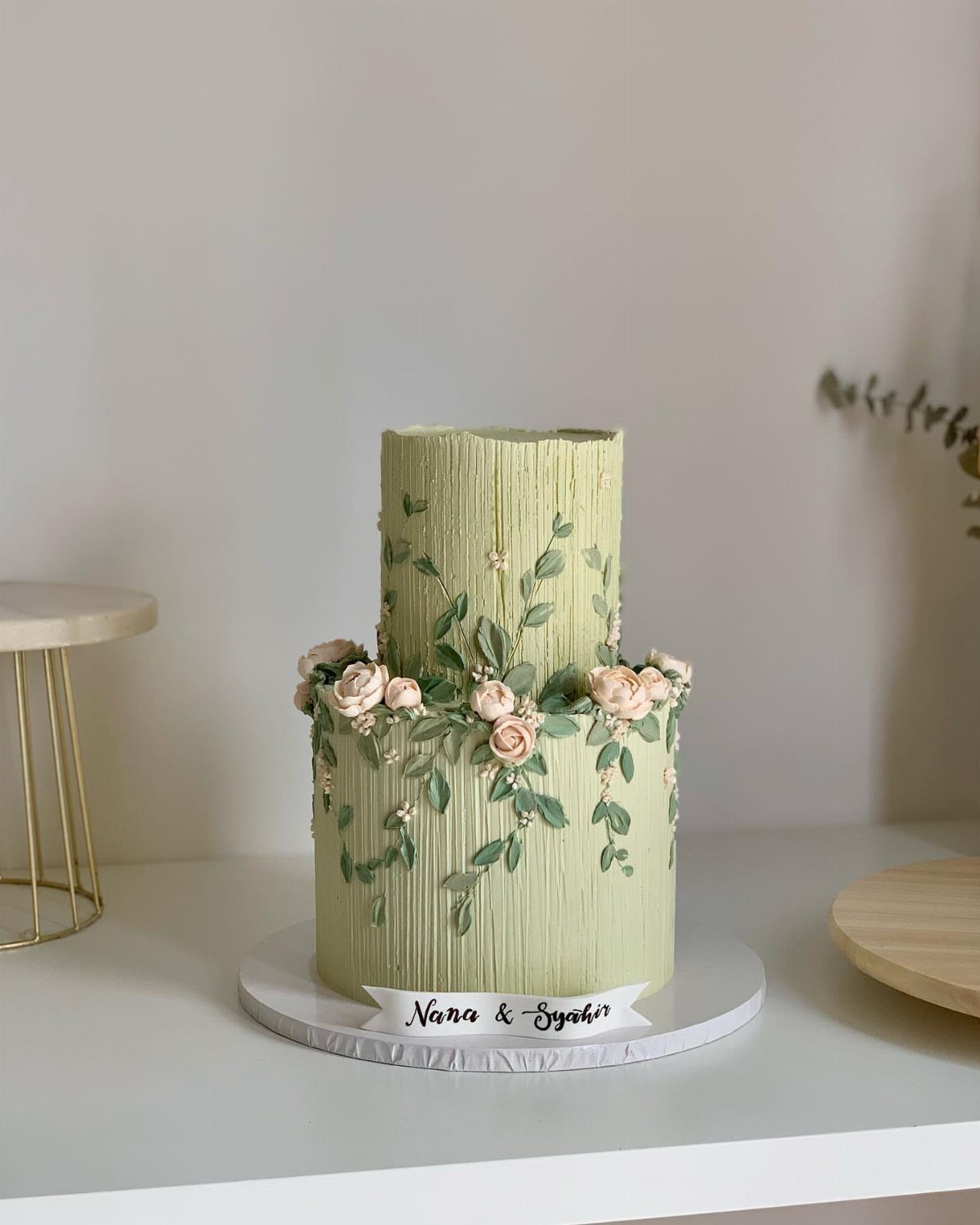 Two-tier sage green ribbed cake decorated with pink roses and green leaf vines.