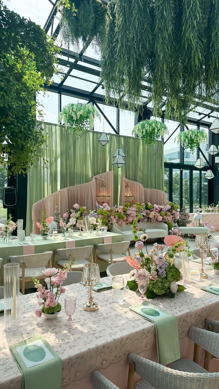 Event tables with sage green napkins and pink florals under hanging greenery installations