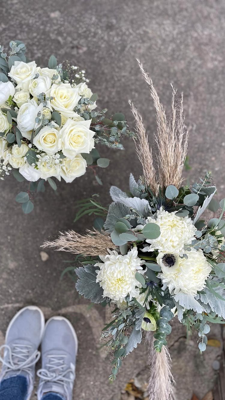 Two white and sage green floral bouquets resting on a grey concrete floor.