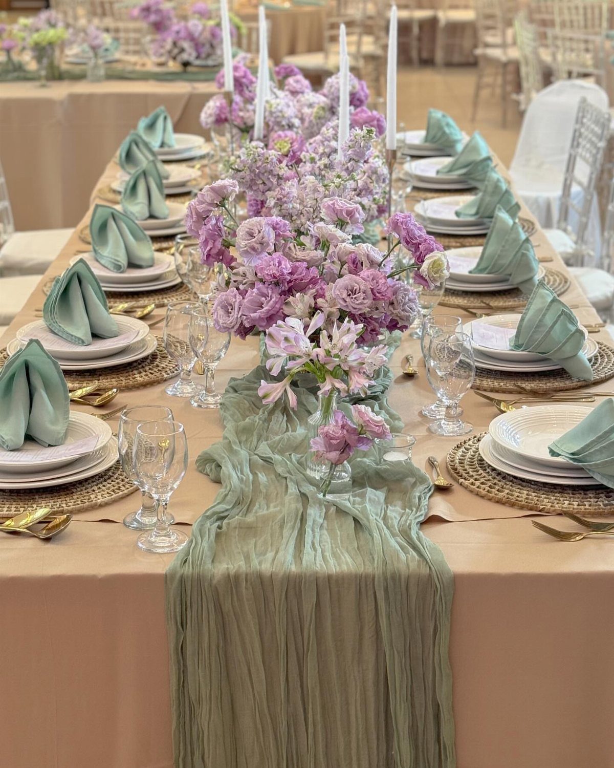 Wedding table with sage green runner, lavender floral centerpieces, and sage green napkins.