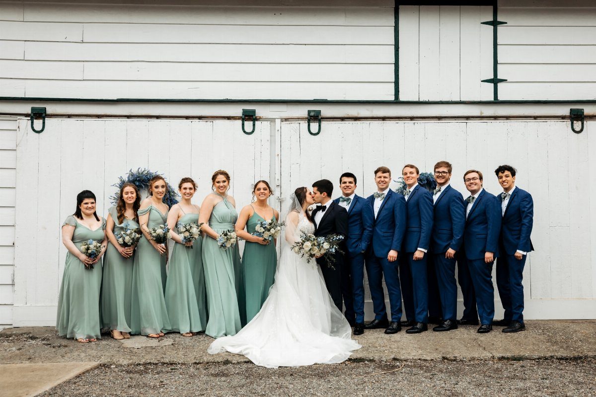 Wedding party with bridesmaids in sage green and groomsmen in navy blue suits.