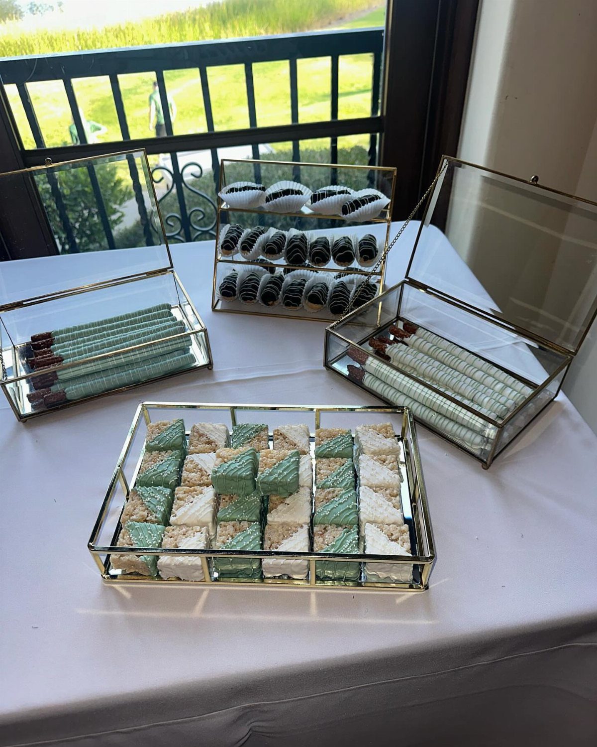 Gold glass trays with sage green desserts and candles on a white table.