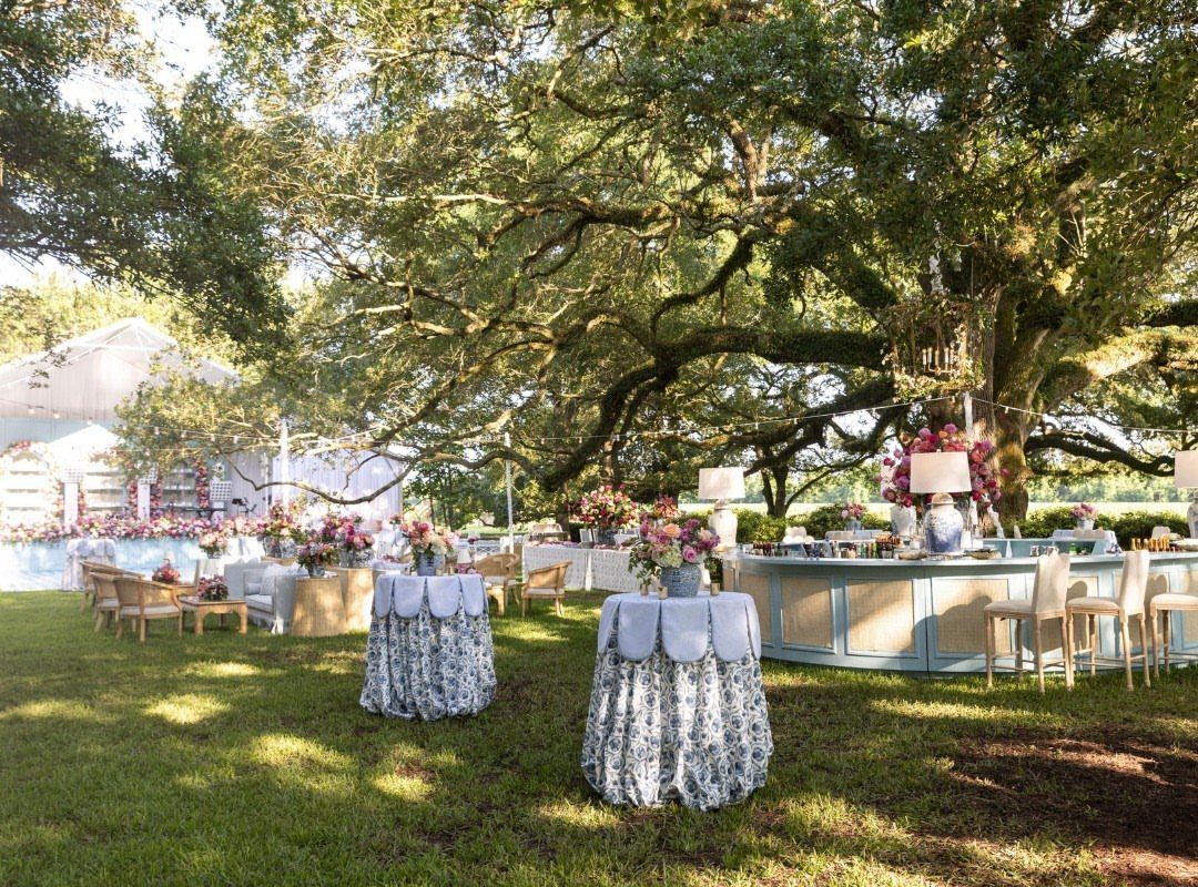 Round tables with blue and white floral-printed linens under a large oak tree.