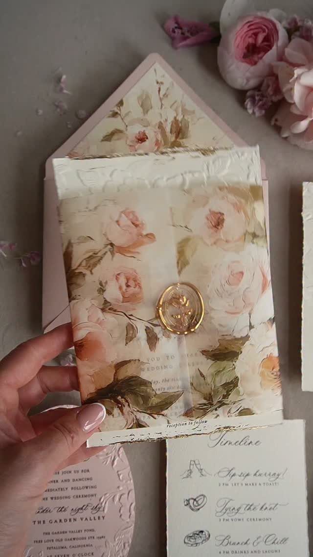 Floral wedding invitation envelope with pink roses and a gold wax seal.