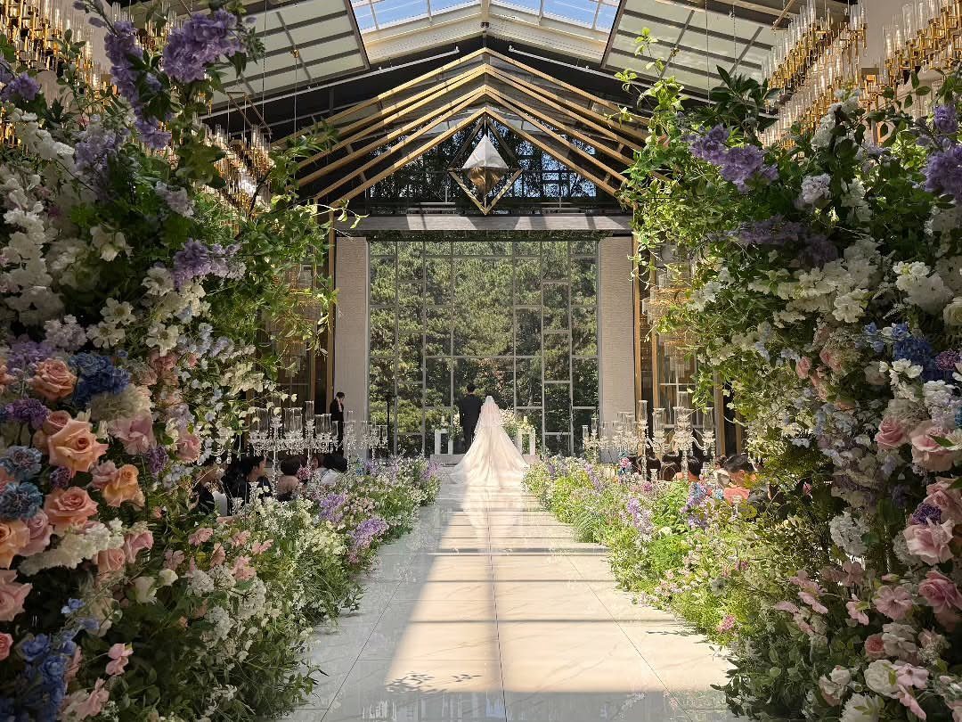 Floral-lined aisle walkway with colorful flowers leading to a bride in a wedding venue.