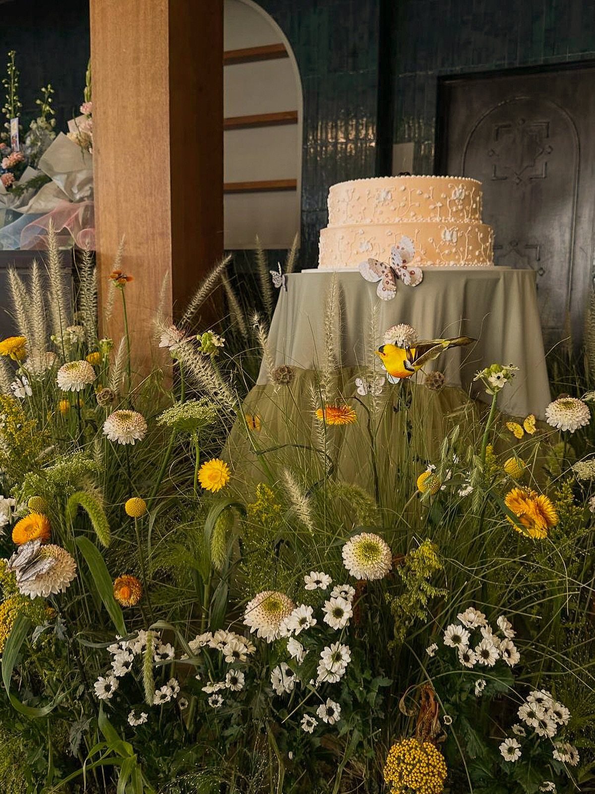 Two-tier white wedding cake on a table surrounded by wild meadow flowers.