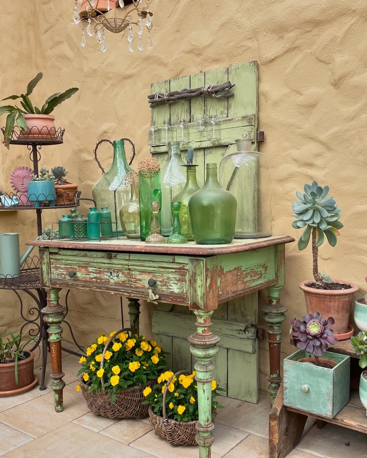 Weathered green vintage wooden table with green glass bottles and potted yellow flowers.