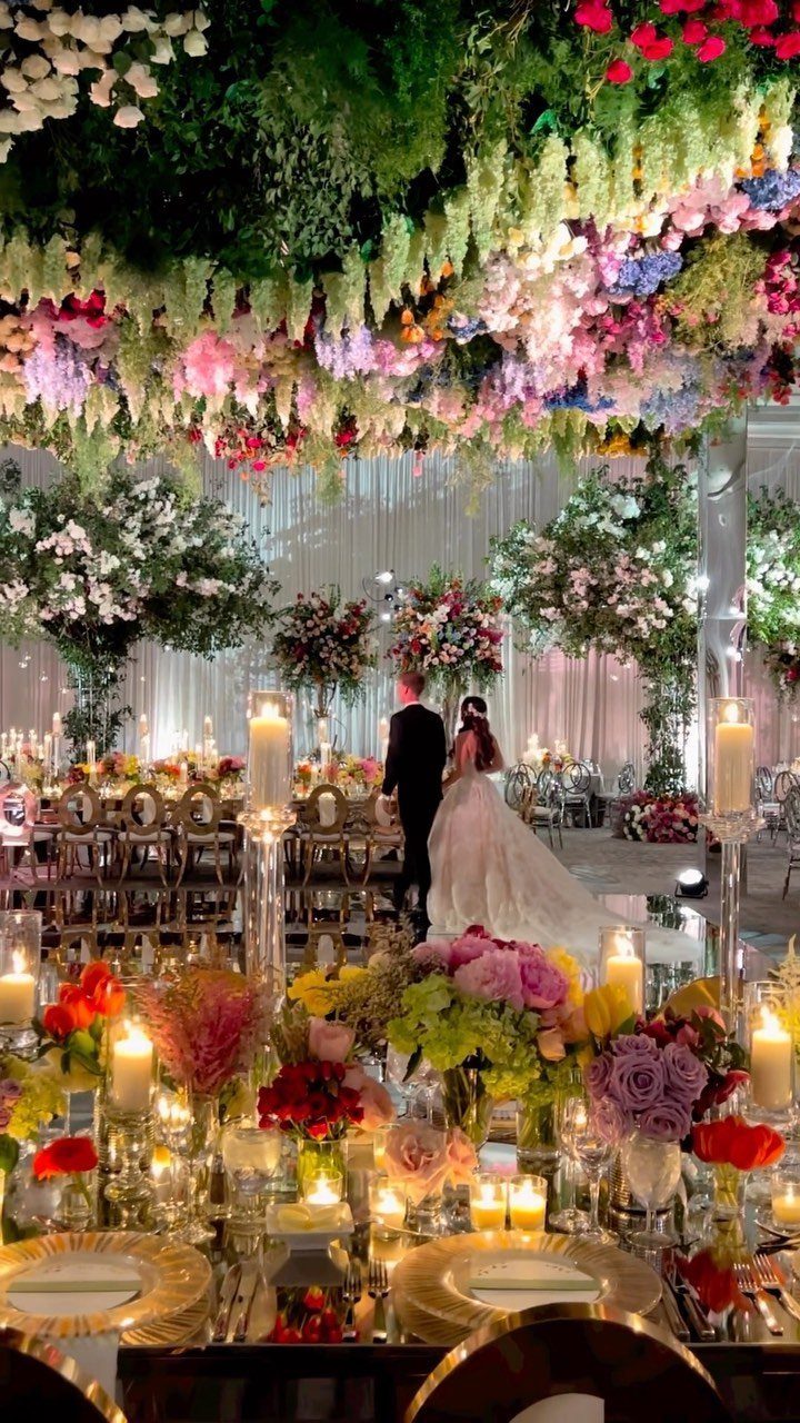 Lavish wedding reception with a ceiling of hanging flowers and candlelit tables.