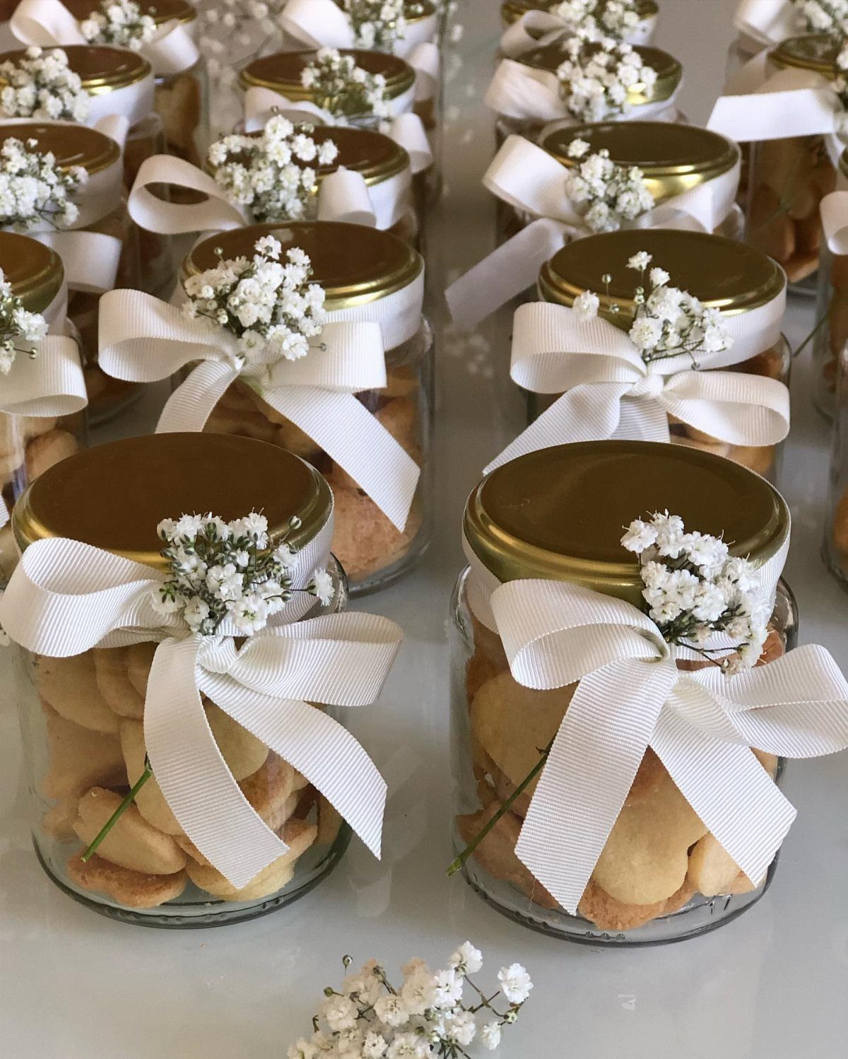 Glass mason jars filled with cookies, tied with white ribbons and baby's breath.