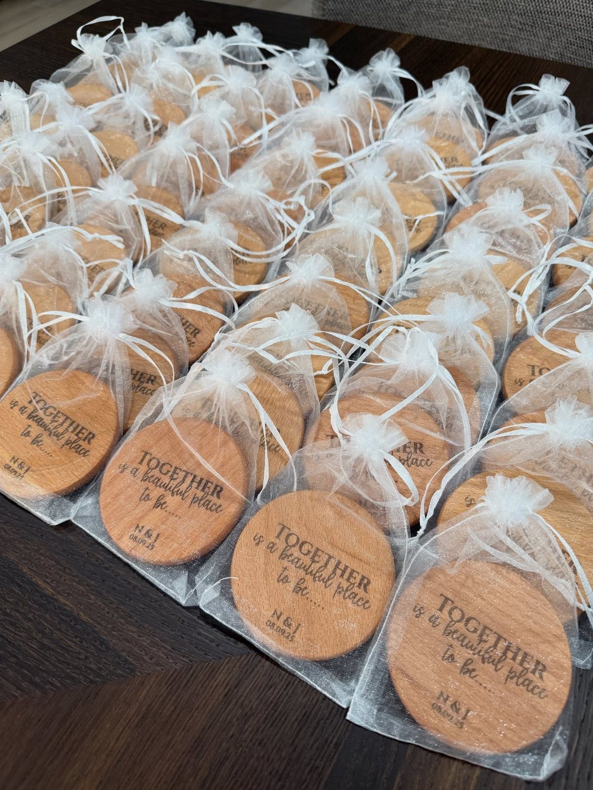 Round wooden engraved coasters wrapped in white organza bags on a dark table.
