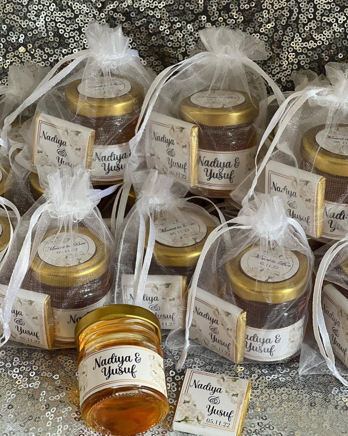 Small honey jars with personalized labels in sheer white organza gift bags.
