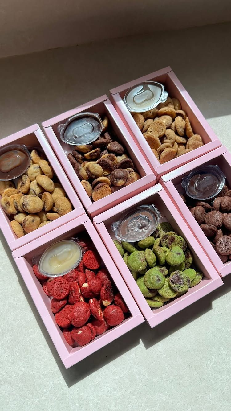 Six pink boxes filled with colorful coated nuts and small dip containers.