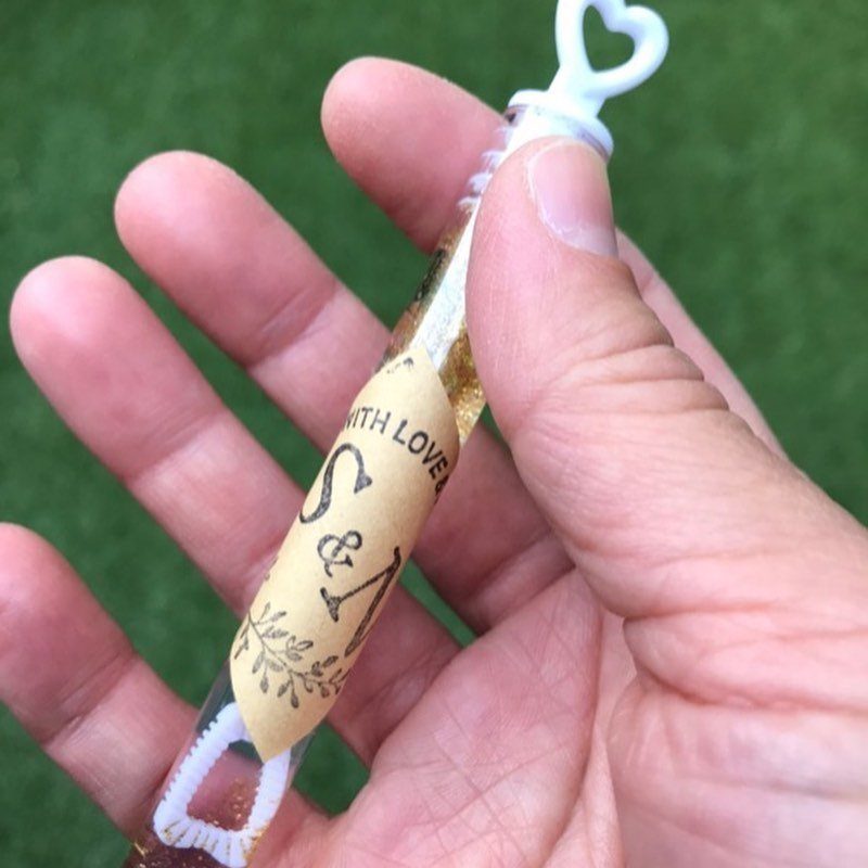 Hand holding a decorated wedding sparkler with gold foil and personalized paper band.