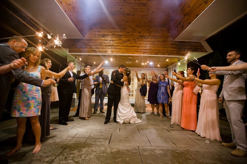 Bride and groom kissing while guests hold lit sparklers in a celebratory circle