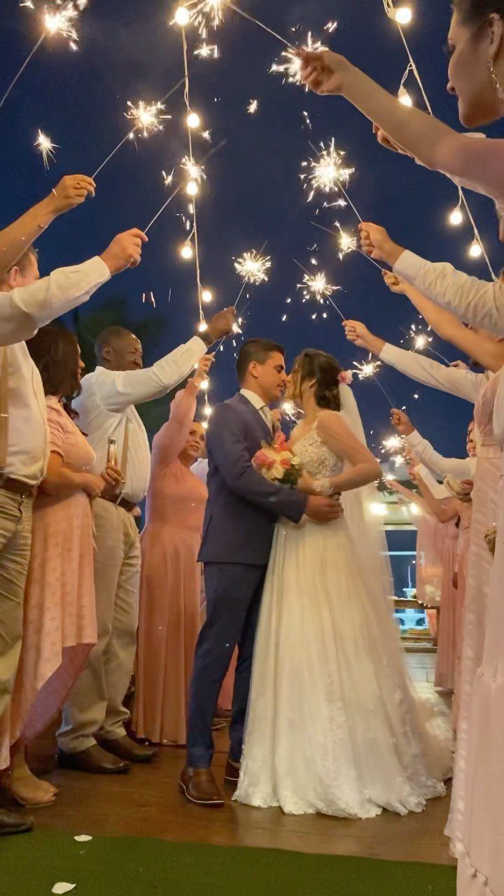 Bride and groom embracing under an arch of lit sparklers held by guests.
