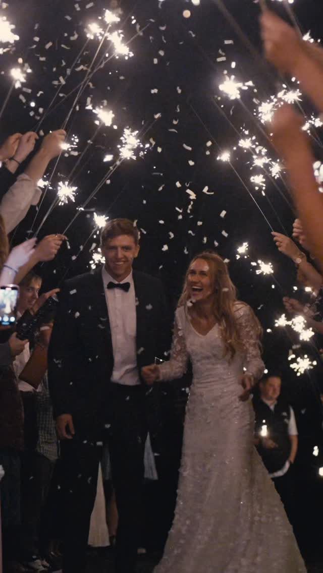 Bride and groom walking through a tunnel of lit sparklers and falling confetti