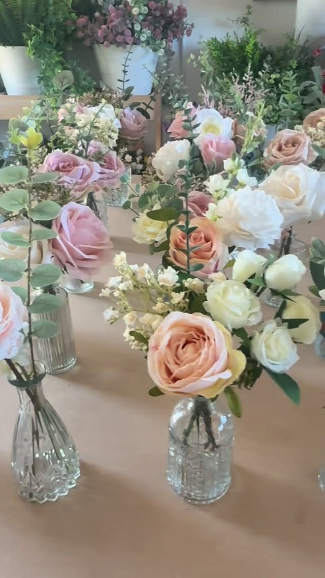 Blush pink and cream roses with sage green leaves in small glass vases.