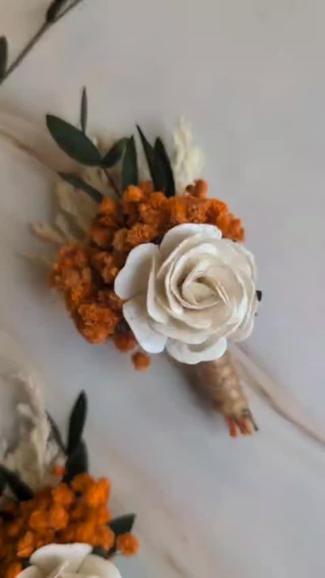 Boutonniere with a white rose and burnt orange flowers on marble background