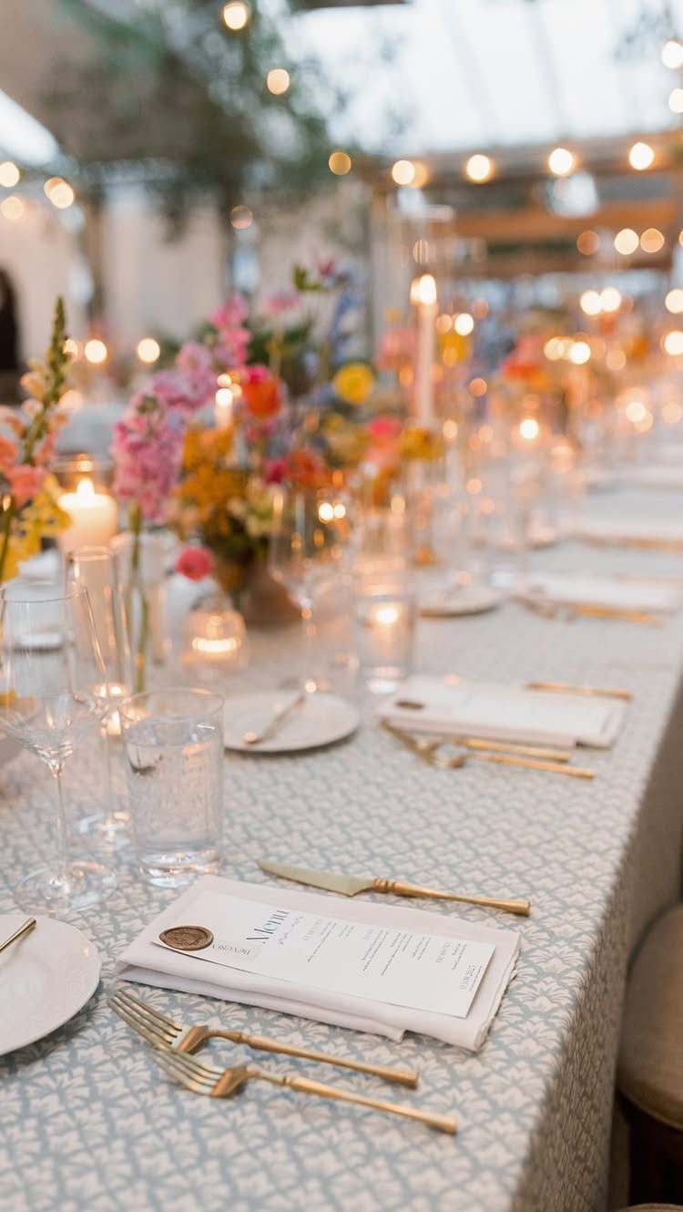 Wedding reception table with light blue linens, gold cutlery, and colorful spring flowers.