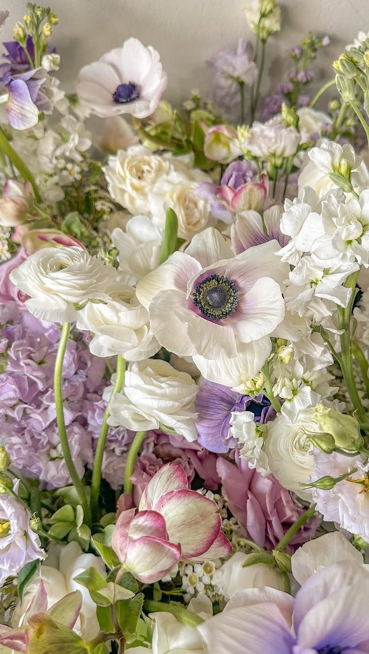 White anemones and cream roses mixed with lilac purple flowers and green leaves.