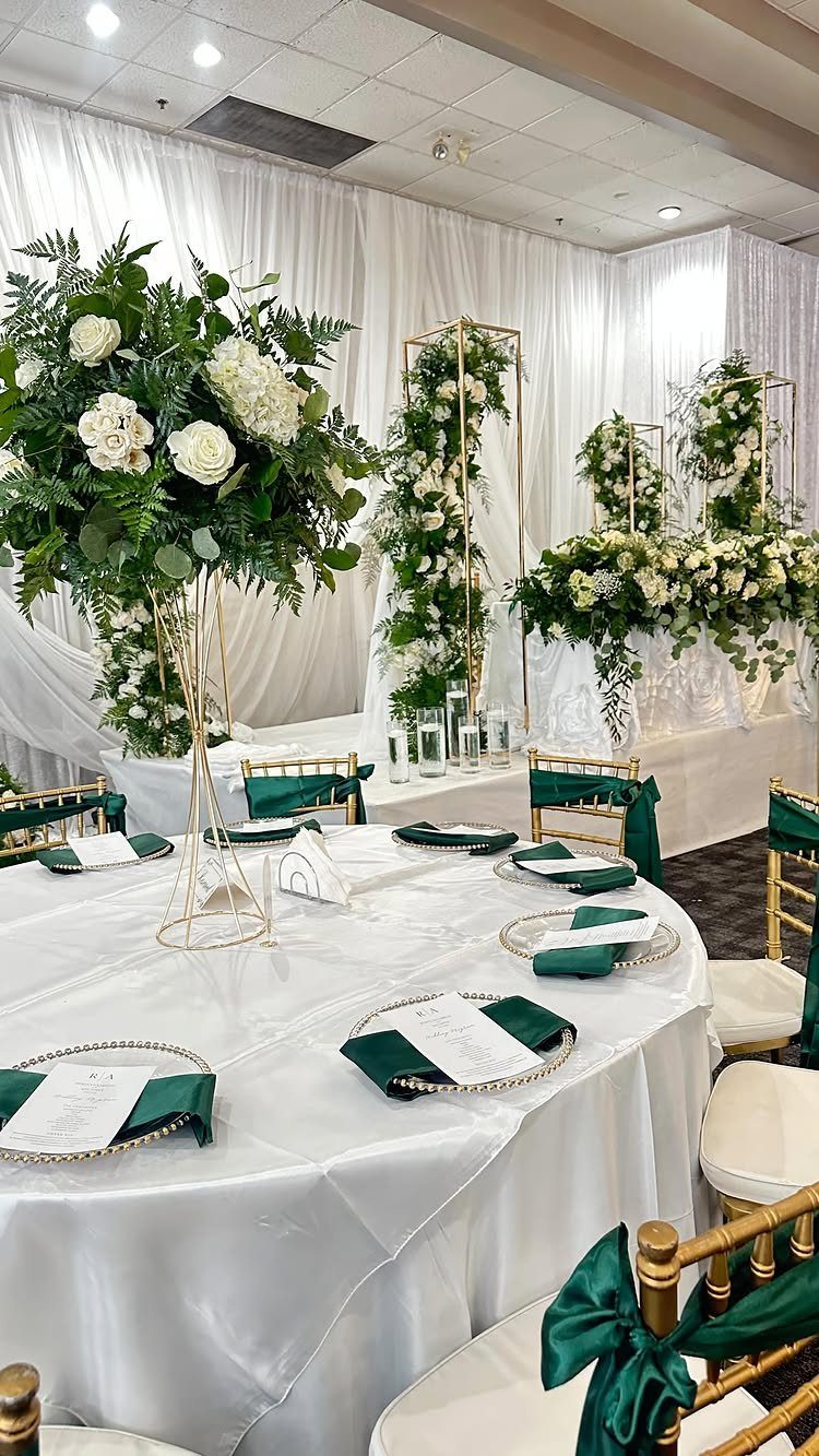 Wedding table setting with white flowers, dark green accents, and gold chairs.