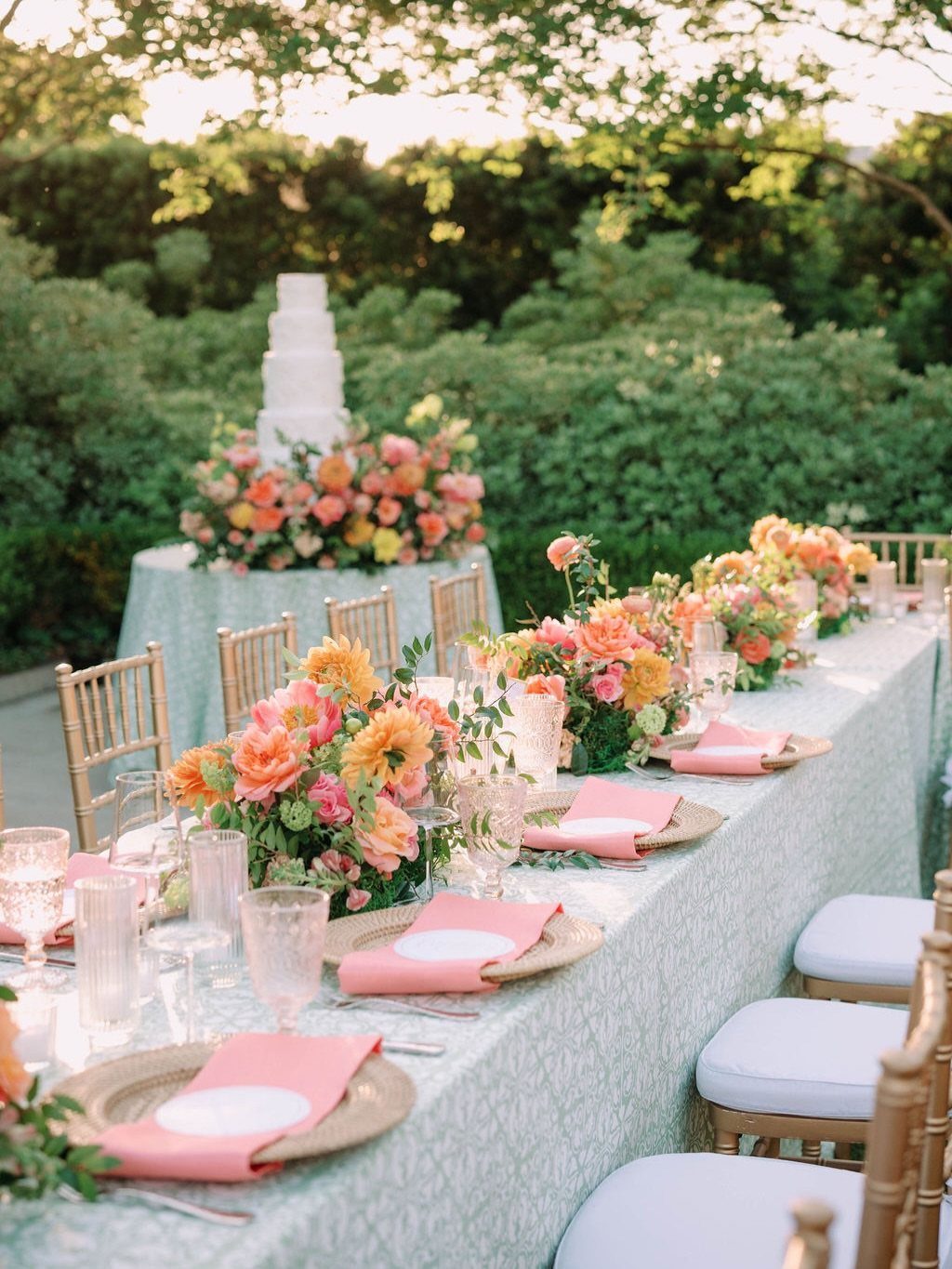 Outdoor wedding table with mint tablecloth, gold chairs, and orange and pink florals.