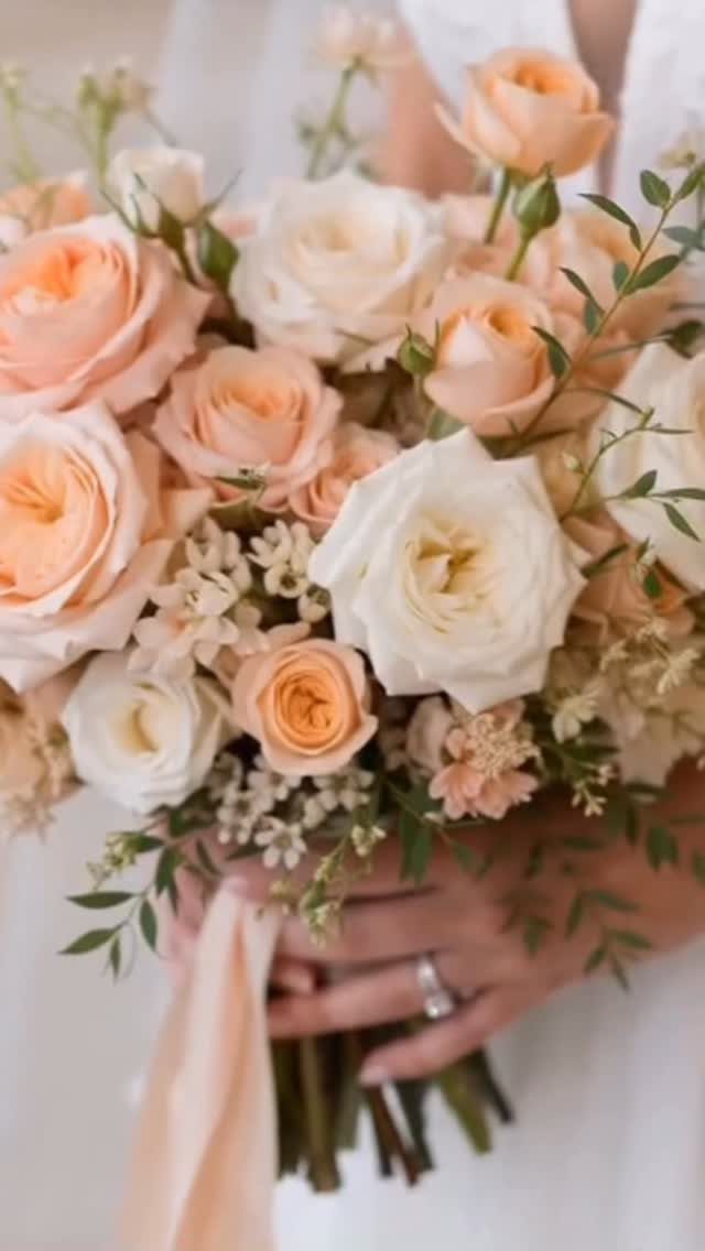 Bridal bouquet with peach and white roses and green foliage held by bride