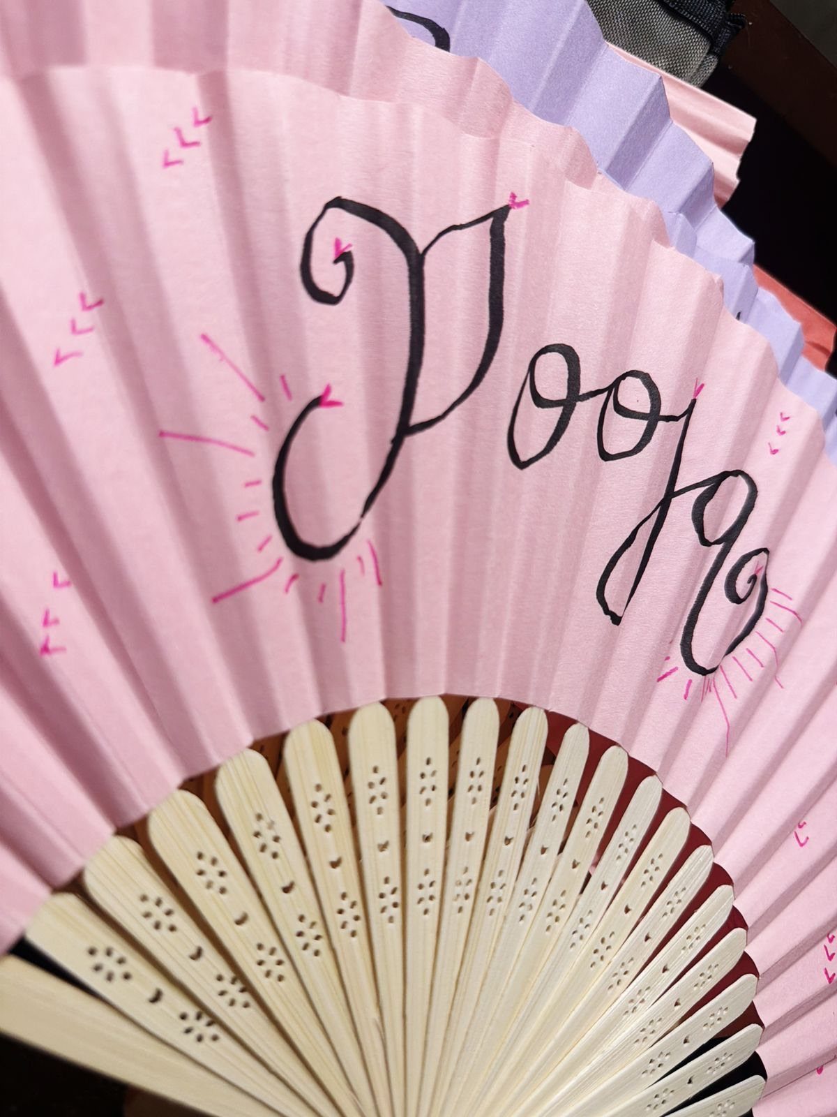 Pink pleated hand fan with black cursive calligraphy and white plastic ribs.