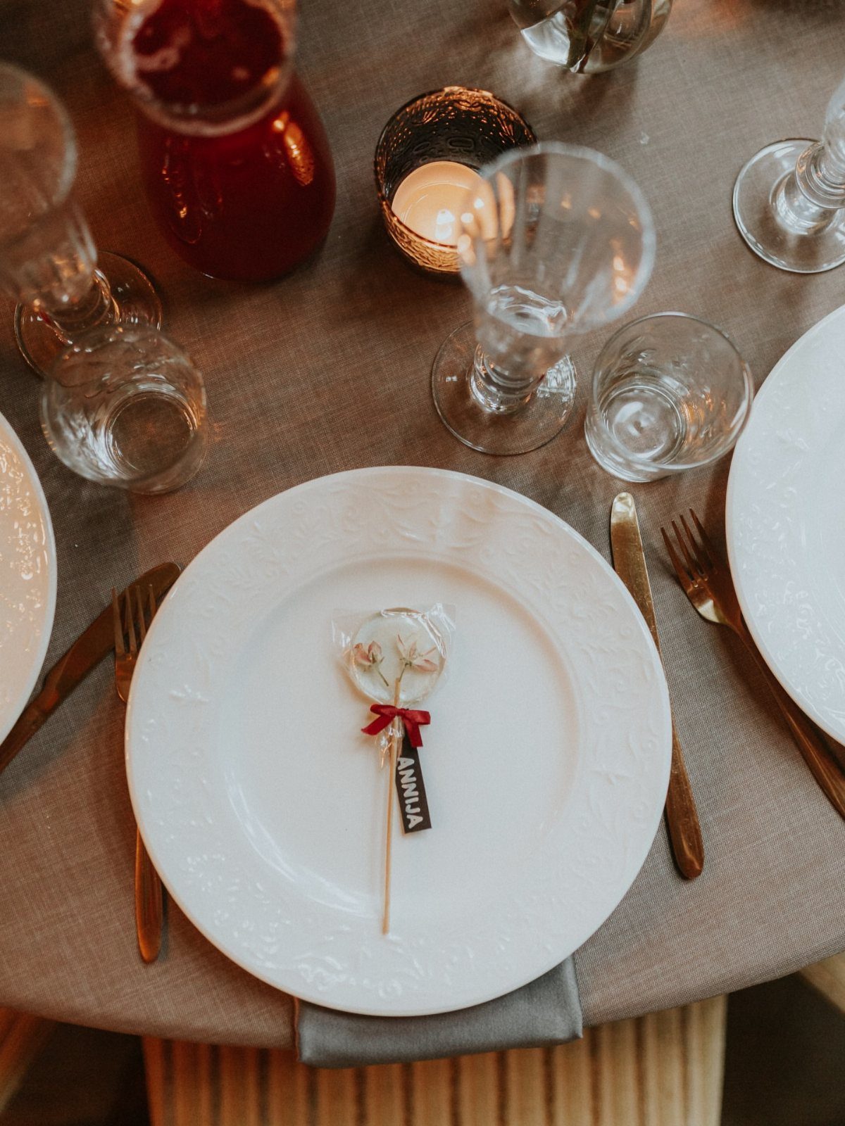 Personalized lollipop with a name tag and red ribbon on a white plate.