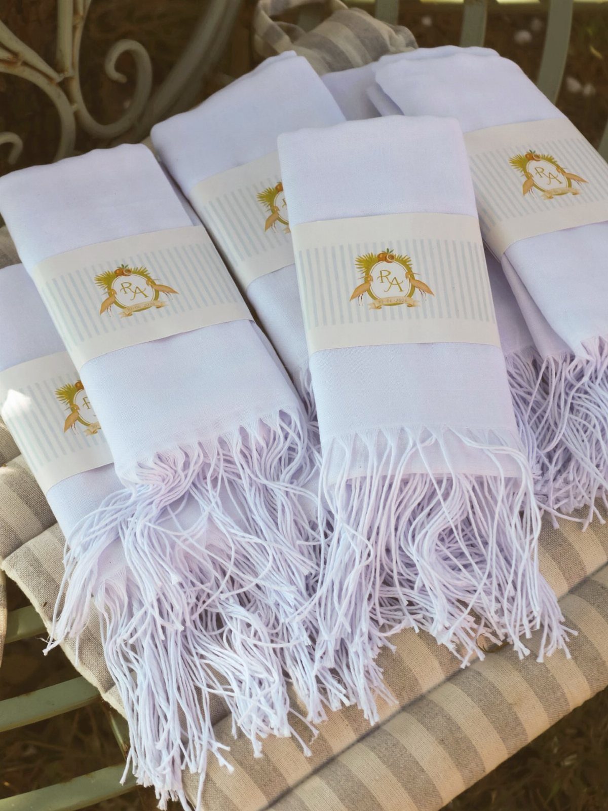 Folded white fringed towels with gold crest paper bands on a striped surface.