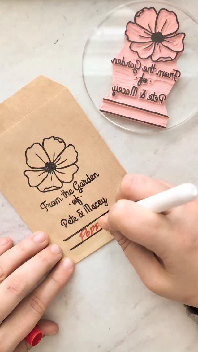 Brown paper seed packets being personalized with a marker and floral stamp.