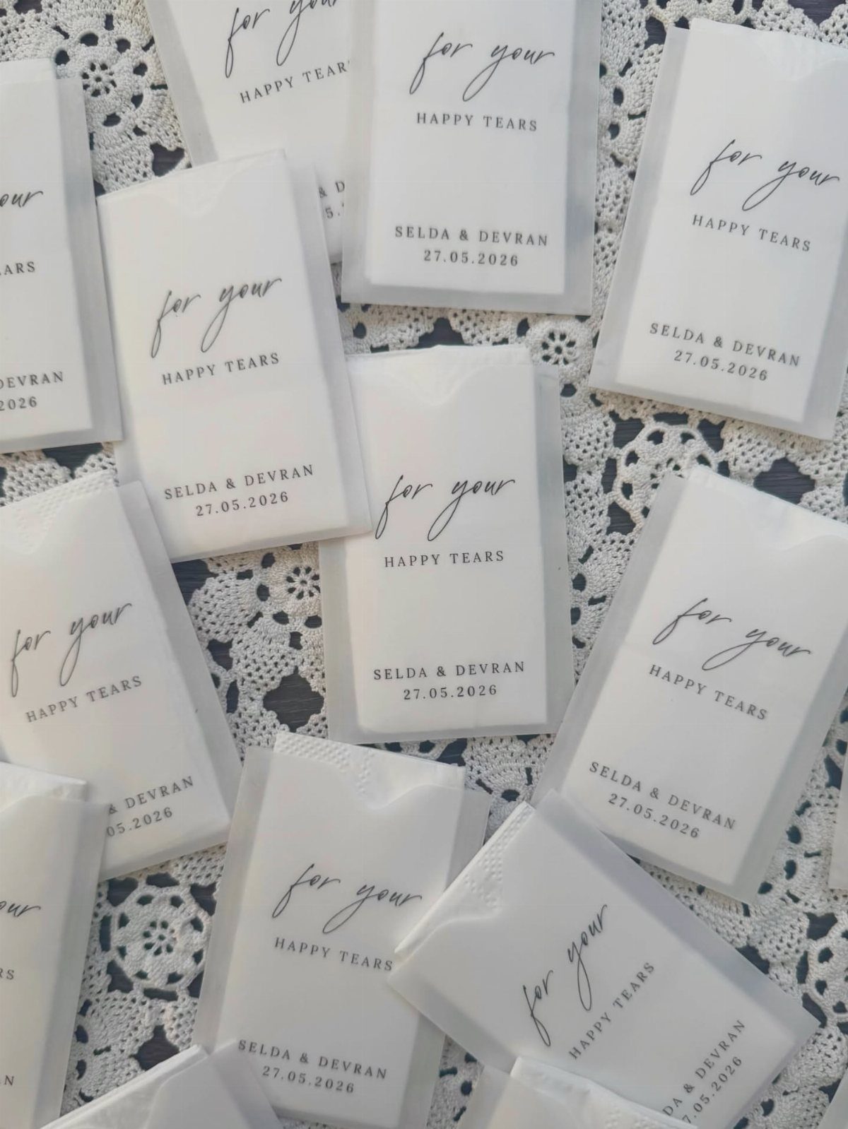 White personalized tissue packets for happy tears resting on a white lace cloth.