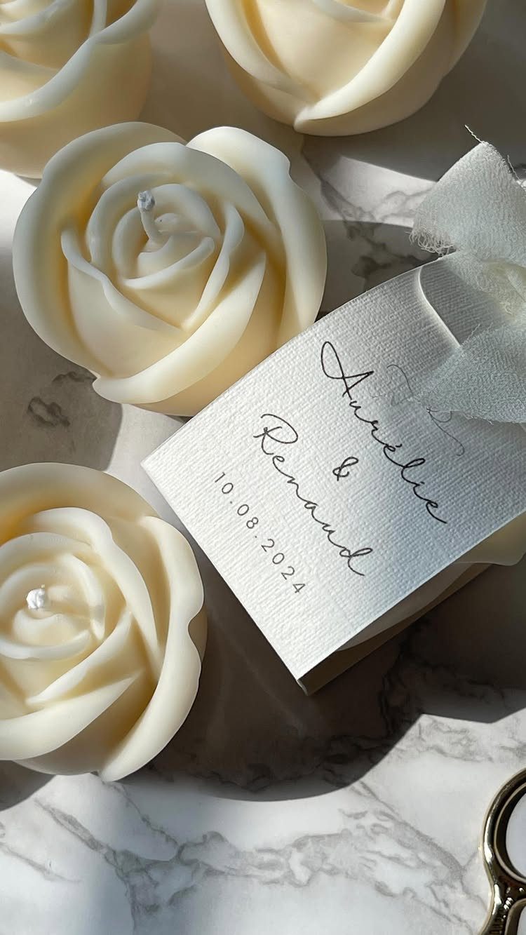Rose-shaped cream candles with a personalized wedding gift tag on marble surface