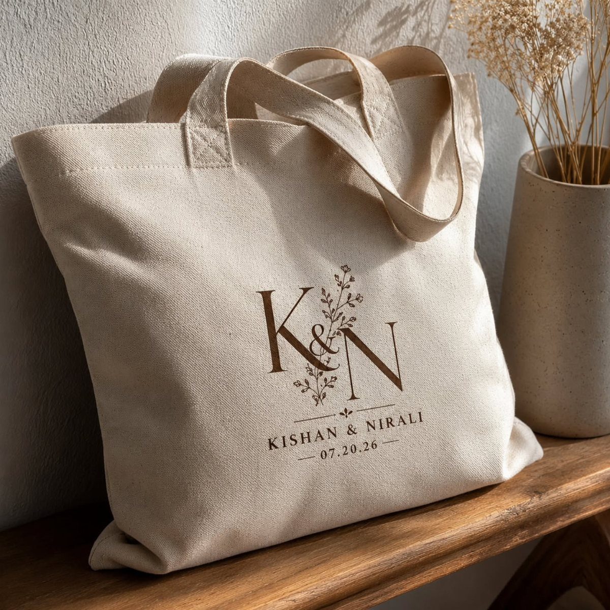 Beige canvas tote bag with personalized names and date on a wooden shelf.