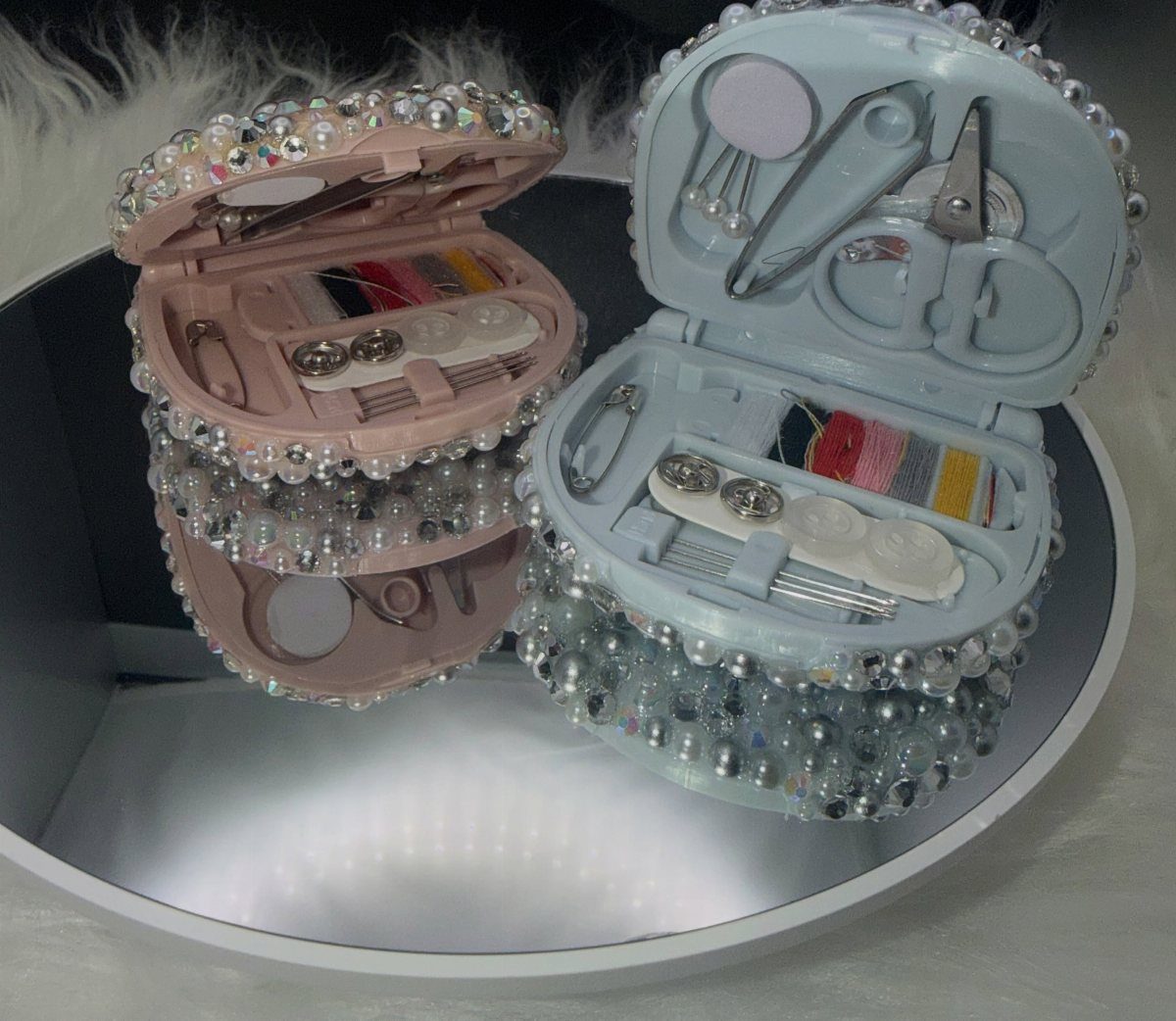 Two pearl-decorated heart-shaped sewing kits in pink and blue on a mirror.